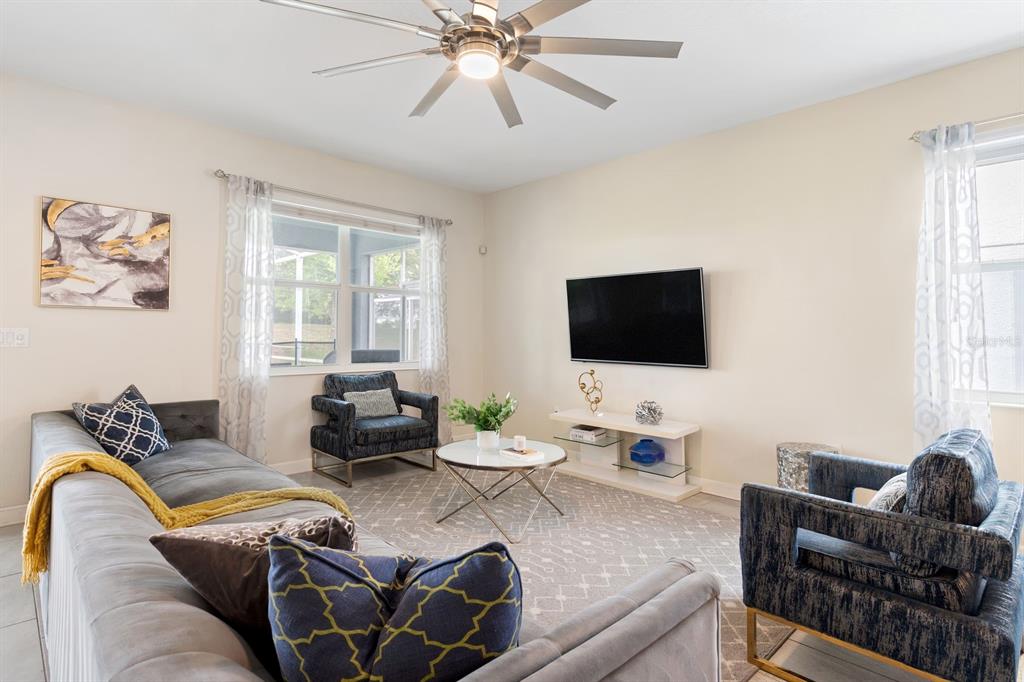 A living room features a gray sectional, two patterned armchairs, a television, and a ceiling fan — 9050 STINGER DRIVE, DAVENPORT, FL