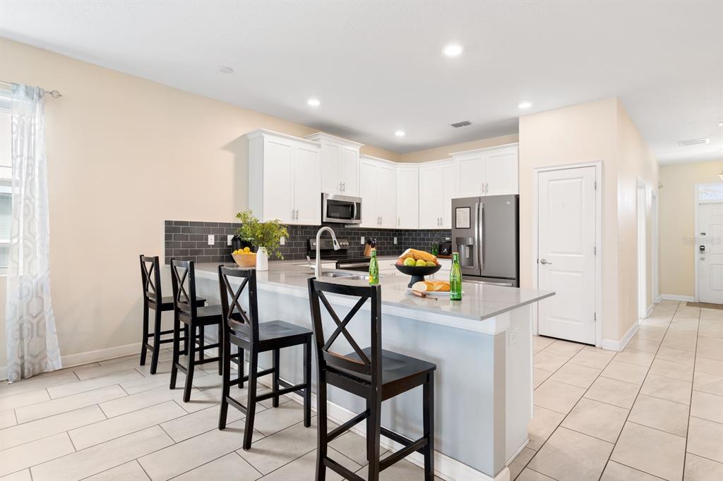 A kitchen features white cabinets, a gray quartz island with bar seating, and dark tile backsplash — 9050 STINGER DRIVE, DAVENPORT, FL
