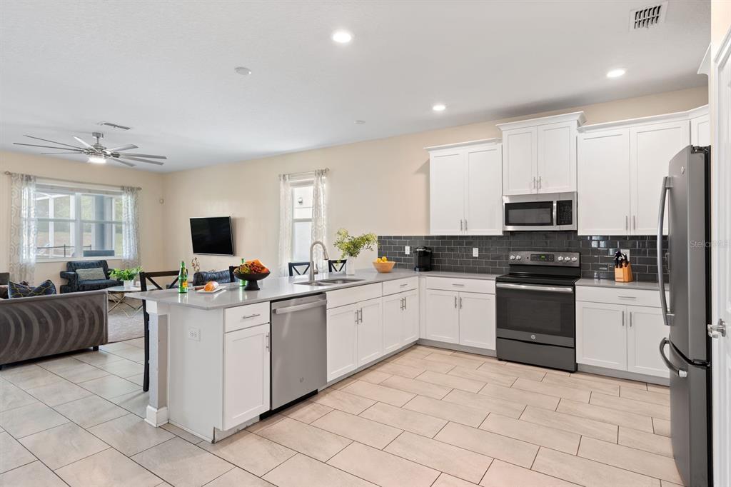 A kitchen with white cabinets, gray countertops, and a dark tile backsplash opens to a living area — 9050 STINGER DRIVE, DAVENPORT, FL