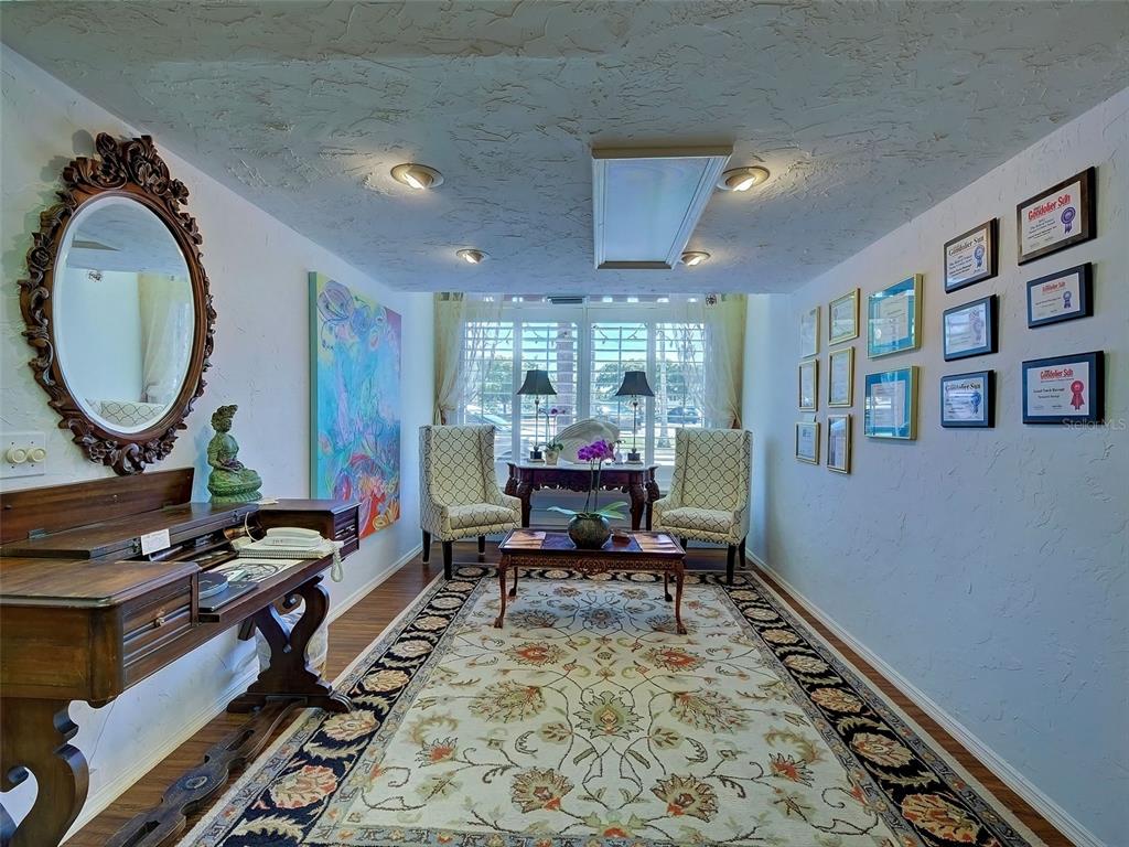 A sunlit sitting room features a patterned area rug, two armchairs, and a wooden desk — 226 TAMPA AVENUE W UNIT 18A, VENICE, FL