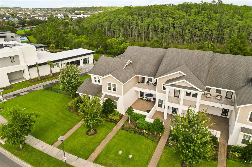 An aerial view of a multi-story townhouse complex with a lawn and adjacent forest — 14229 KELLOGG AVENUE, ORLANDO, FL
