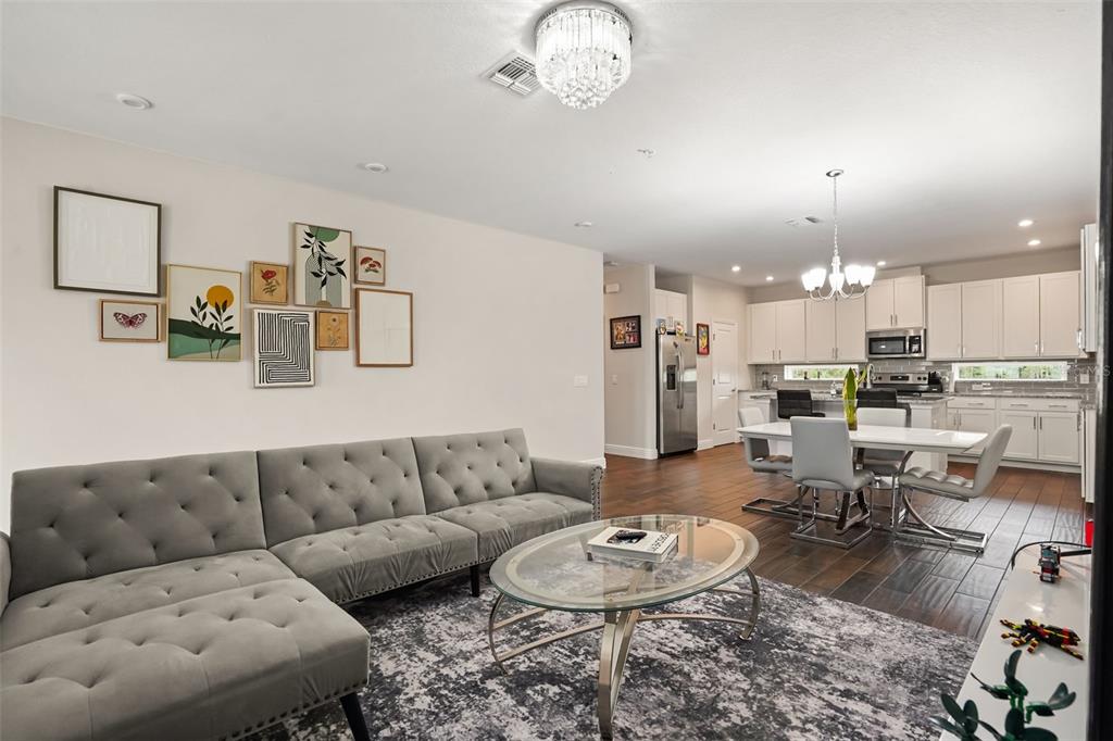 A living room with a grey tufted sectional sofa opens to a kitchen and dining area — 14229 KELLOGG AVENUE, ORLANDO, FL