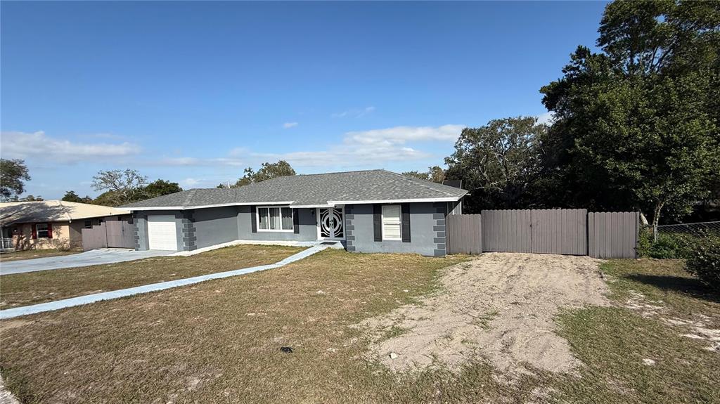 A gray single-story house features a white front door, a garage, and a wooden fence — 7223 TARRYTOWN DRIVE, SPRING HILL, FL
