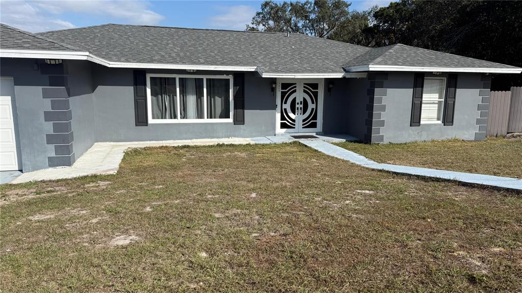 A gray single-story house features a white double front door and a gray shingled roof — 7223 TARRYTOWN DRIVE, SPRING HILL, FL
