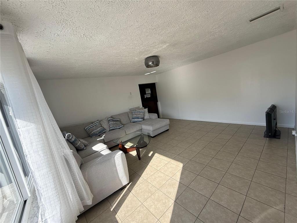 A living room features light-colored tile flooring, a sectional sofa, and a glass coffee table — 7223 TARRYTOWN DRIVE, SPRING HILL, FL