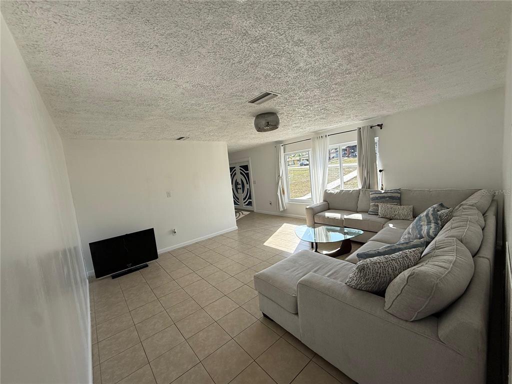 A living room features light tile flooring, a large sectional sofa, and a television — 7223 TARRYTOWN DRIVE, SPRING HILL, FL
