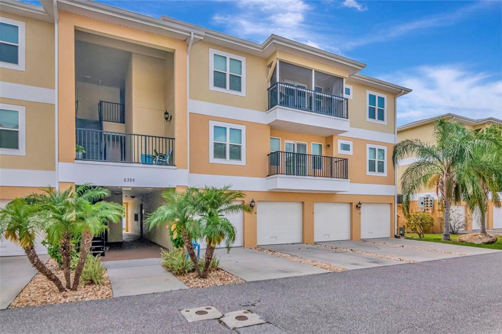 A three-story apartment building features a ground-level parking area, balconies, and palm trees — 6395 BANYAN BOULEVARD UNIT 303, NEW PORT RICHEY, FL