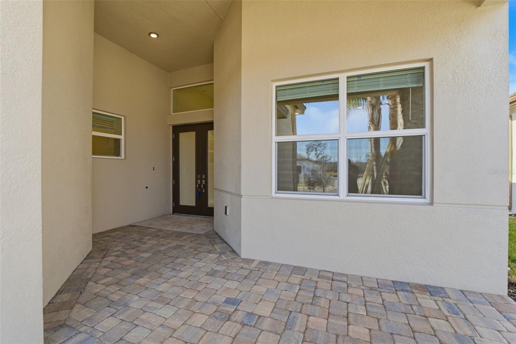 A covered entryway with paver flooring, a dark front door, and a large window — 32623 NEROLI STREET, WESLEY CHAPEL, FL