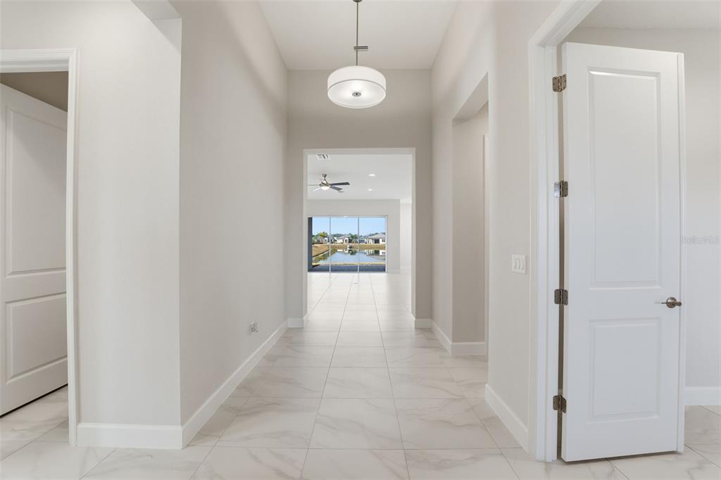 A bright hallway with light tile flooring leads toward a living area with water views — 32623 NEROLI STREET, WESLEY CHAPEL, FL