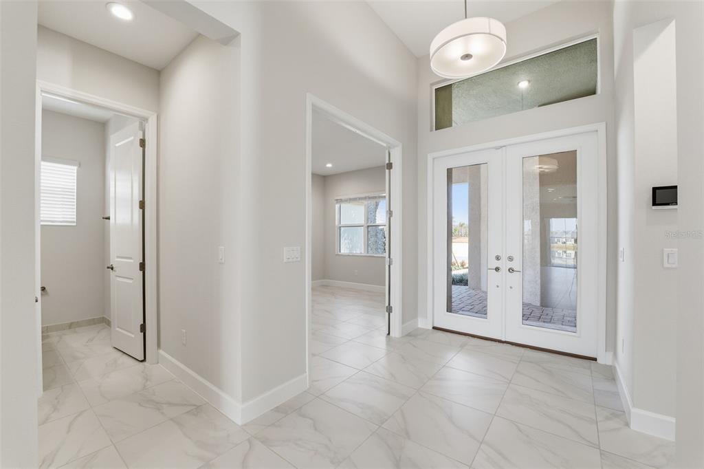 A bright entryway features white tile flooring, double glass front doors, and a modern light fixture — 32623 NEROLI STREET, WESLEY CHAPEL, FL