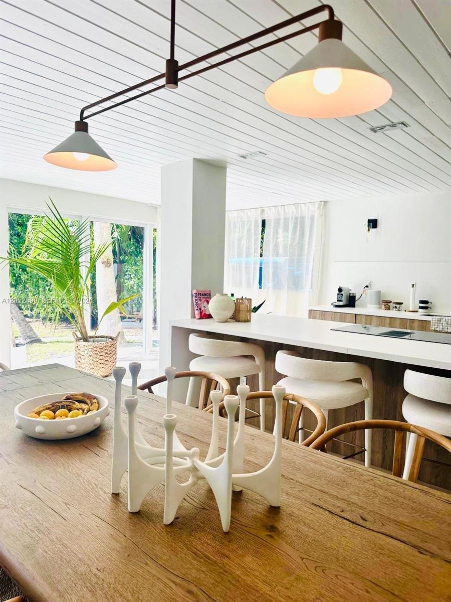 A dining area and kitchen feature a wooden table, white stools, and modern pendant lighting — 8300 Hawthorne Ave, Miami Beach FL 33141, MIAMI BEACH, FL