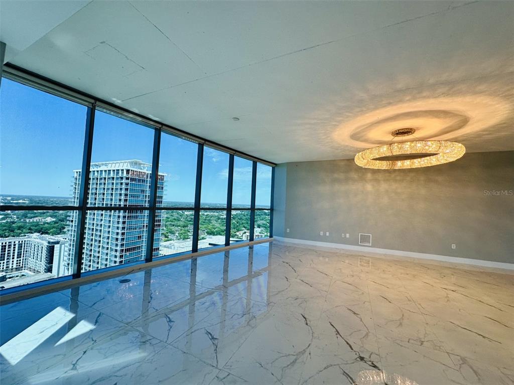 A modern, empty room features floor-to-ceiling windows, marble-patterned tile flooring, and a circular chandelier — 111-3 WASHINGTON STREET, ORLANDO, FL