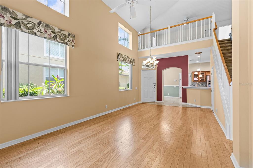 An empty living room with hardwood floors, a vaulted ceiling, and an open loft balcony — 3350 COVERED BRIDGE DRIVE W, DUNEDIN, FL