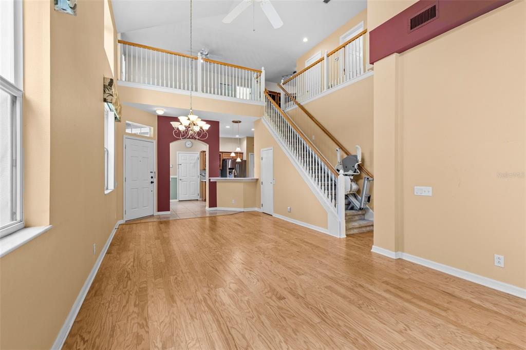 A spacious living room features light wood flooring, a staircase with a lift, and a balcony — 3350 COVERED BRIDGE DRIVE W, DUNEDIN, FL