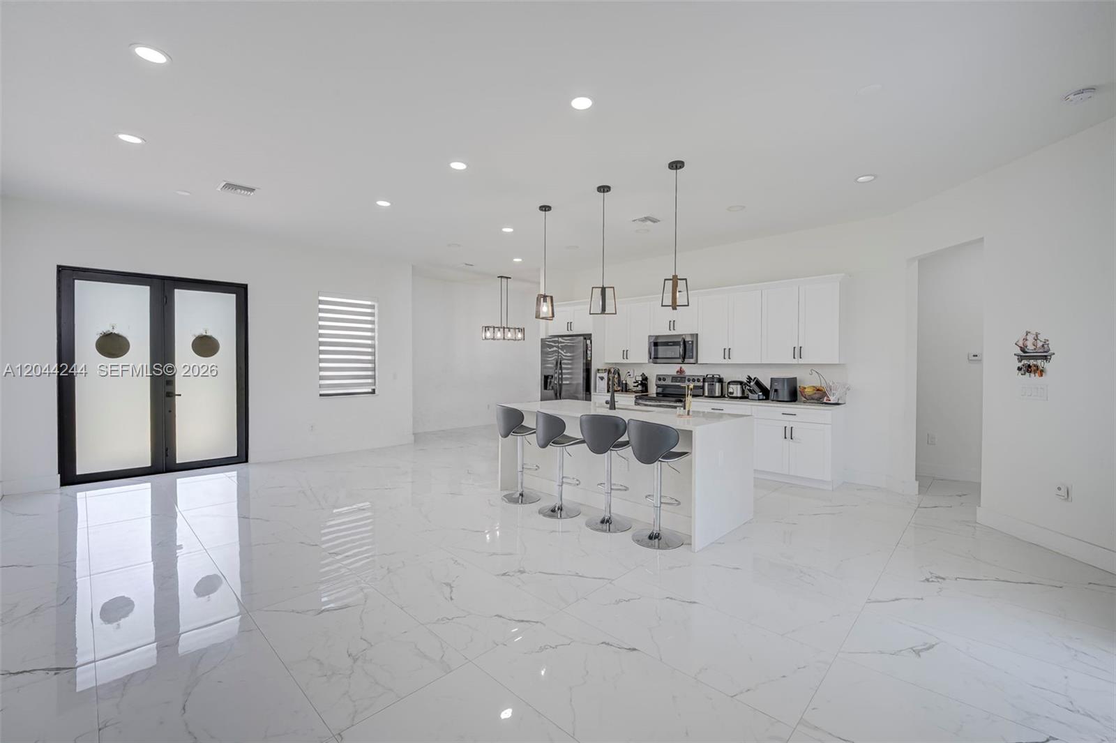 A modern kitchen features white cabinetry, a central island with bar stools, and marble flooring — 7834 14TH PL, La Belle FL 33935, LA BELLE, FL