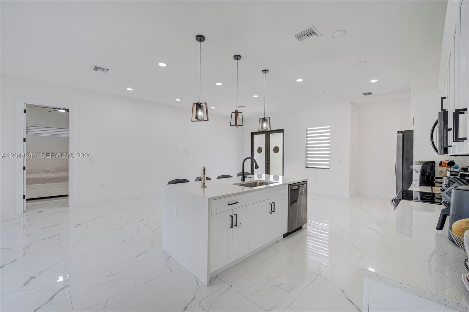 A modern white kitchen features a central island with a sink and three pendant lights — 7834 14TH PL, La Belle FL 33935, LA BELLE, FL