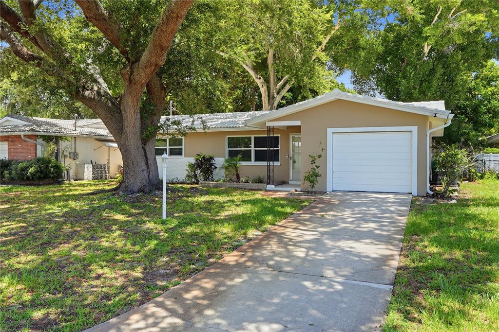 A single-story house with a tan exterior, a white garage door, and a large oak tree — 2437 RUTLAND LANE, CLEARWATER, FL