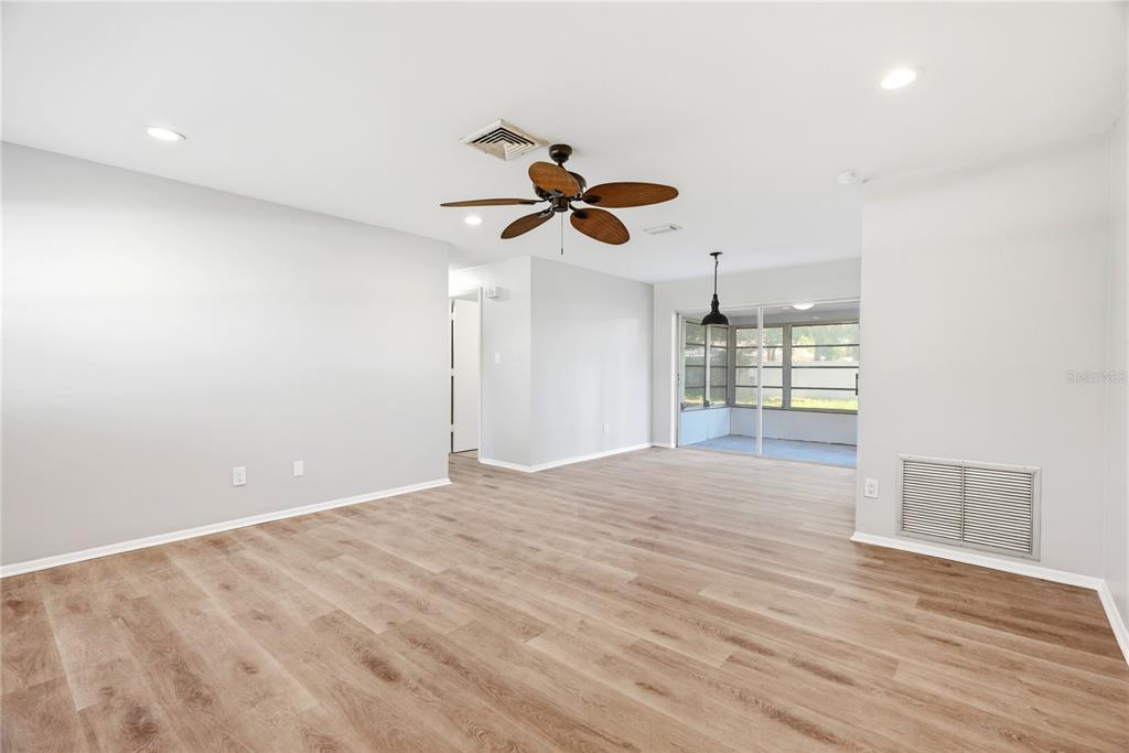 A bright, empty living room features light wood-look flooring, a ceiling fan, and sliding glass doors — 2437 RUTLAND LANE, CLEARWATER, FL