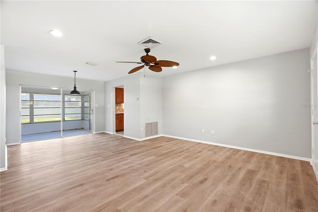 An empty living room features light wood-look flooring, a ceiling fan, and a sliding glass door — 2437 RUTLAND LANE, CLEARWATER, FL