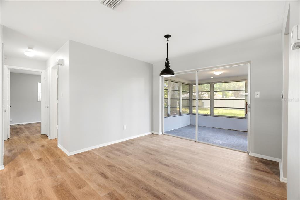 A dining area with light wood flooring, a pendant light, and sliding doors to a porch — 2437 RUTLAND LANE, CLEARWATER, FL