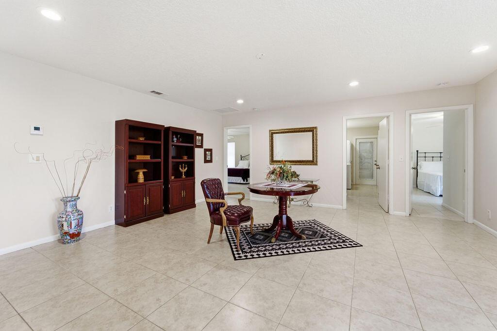 A spacious room with tile flooring, a round wooden table, a chair, and dark bookshelves — 5562 Reynolds Road, Lake Worth FL 33449, LAKE WORTH, FL