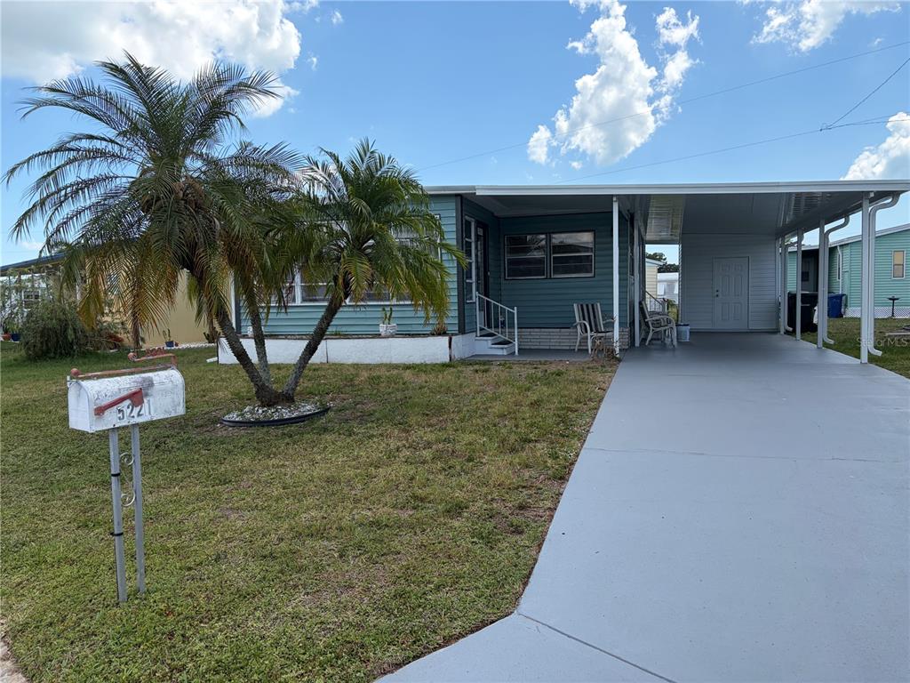 A teal mobile home features a palm tree in the yard and a covered carport — 5221 BEECHMONT AVENUE, SARASOTA, FL