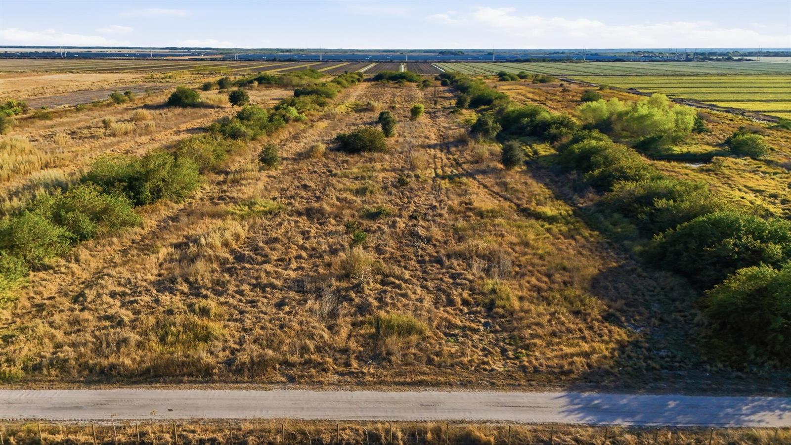 An aerial view shows a large, rectangular grassy lot bordered by a road and trees — 7081 6th Avenue, FL 33935, FL