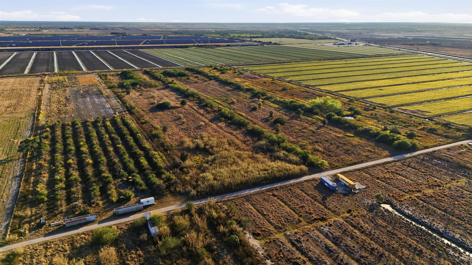 An aerial view shows agricultural fields, a solar farm, and shipping containers on a dirt road — 7081 6th Avenue, FL 33935, FL