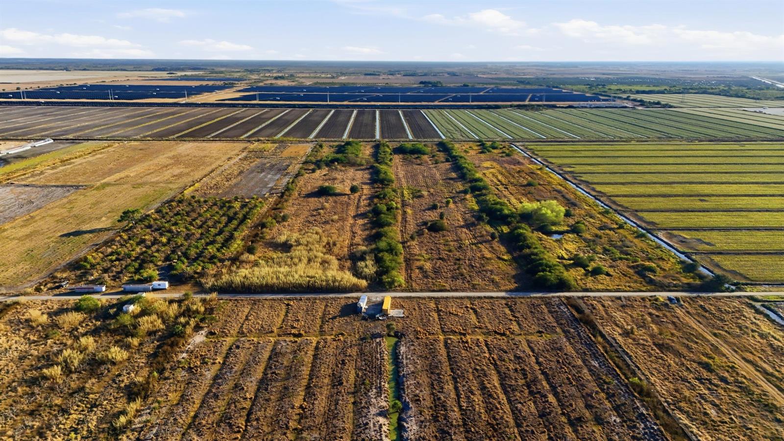 An aerial view shows a large agricultural landscape with fields, irrigation channels, and solar panels — 7081 6th Avenue, FL 33935, FL