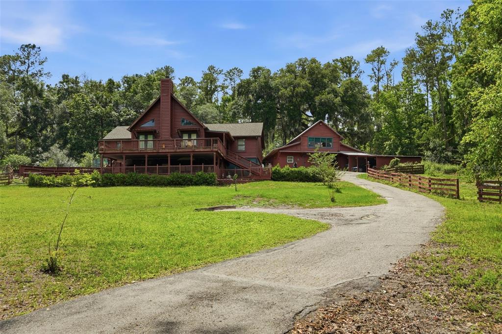 A red wooden house with a large deck and a detached garage sits on a lawn — 24050 WINDING CREEK DRIVE, BROOKSVILLE, FL