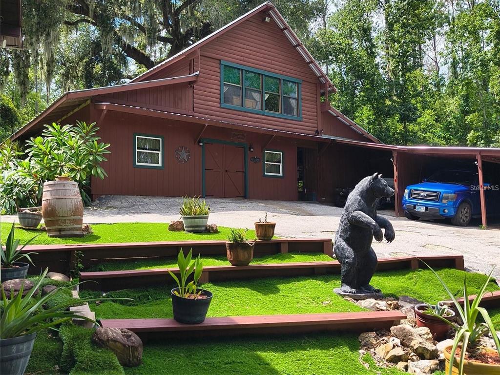 A brown barn-style house with a carport, a bear statue, and tiered landscaping — 24050 WINDING CREEK DRIVE, BROOKSVILLE, FL
