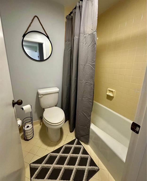 A bathroom features a toilet, a bathtub with a gray curtain, and a round wall mirror — 19660 SW 83RD PLACE ROAD UNIT C17, DUNNELLON, FL
