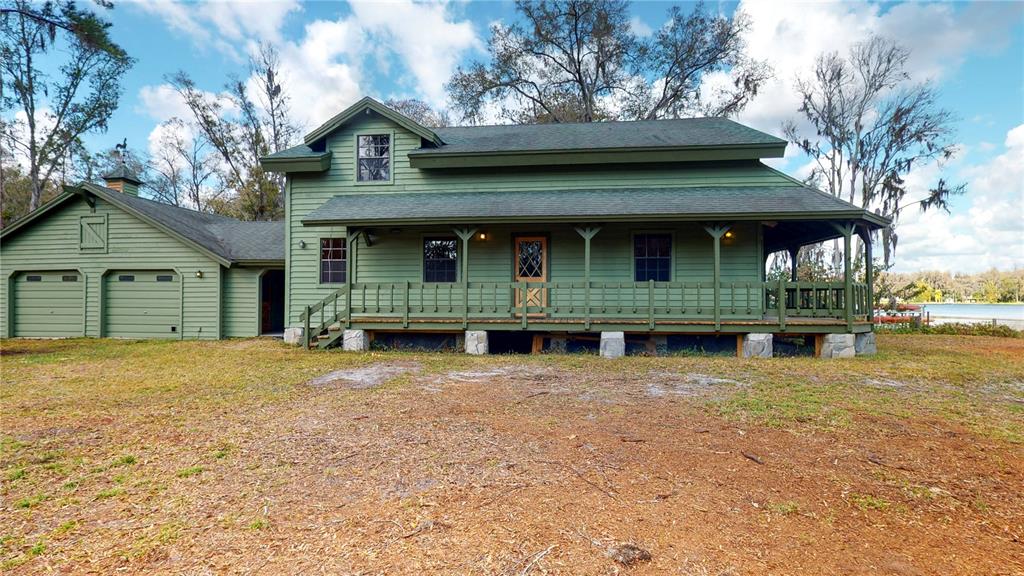 A green two-story house with a wrap-around porch and attached garage sits on grass — 19803 READING ROAD, LUTZ, FL