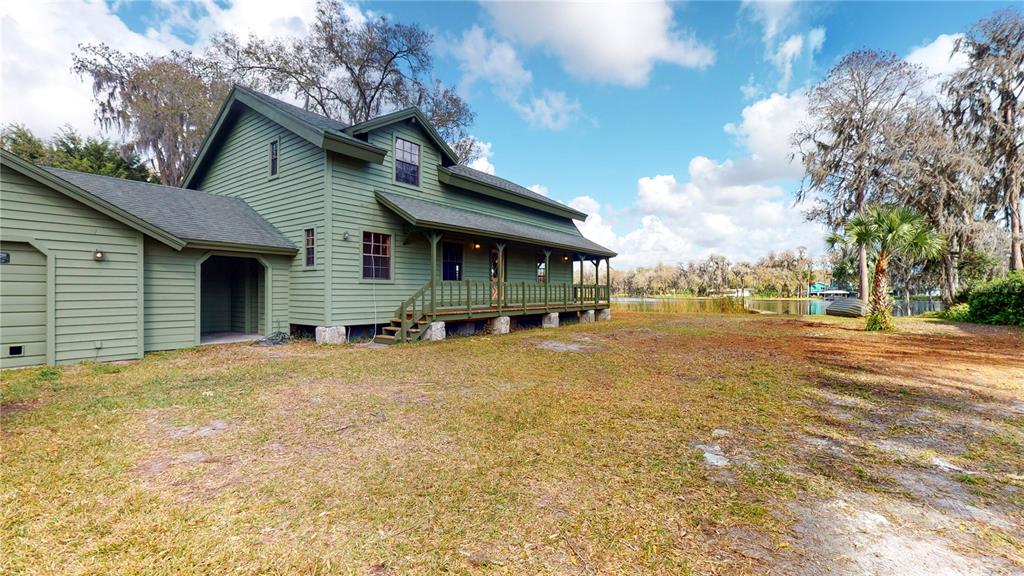 A green two-story house with a porch sits on a grassy lot near a lake — 19803 READING ROAD, LUTZ, FL