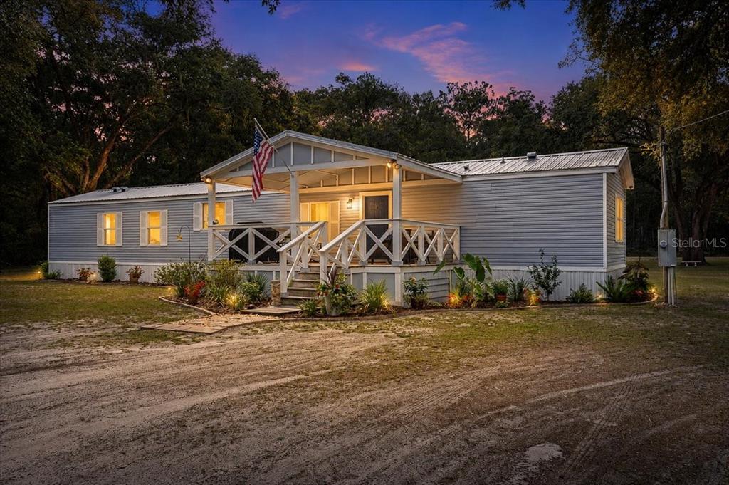 A single-story manufactured home with a covered front porch and metal roof at dusk — 16221 SW 67TH PLACE, ARCHER, FL