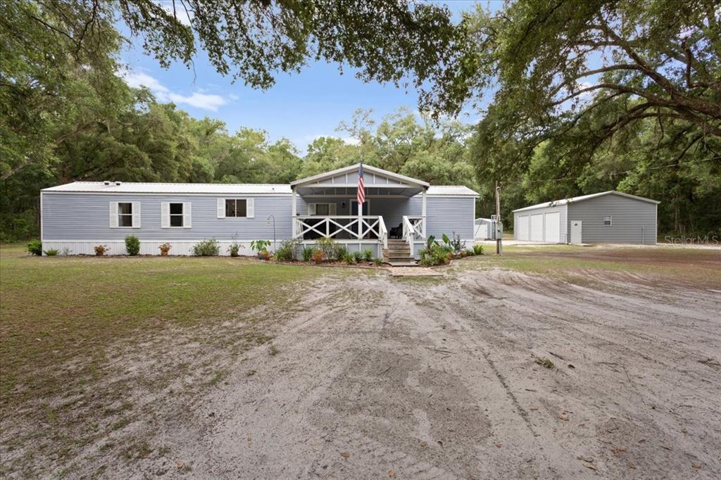 A light blue manufactured home with a front porch and detached garage sits on a lot — 16221 SW 67TH PLACE, ARCHER, FL