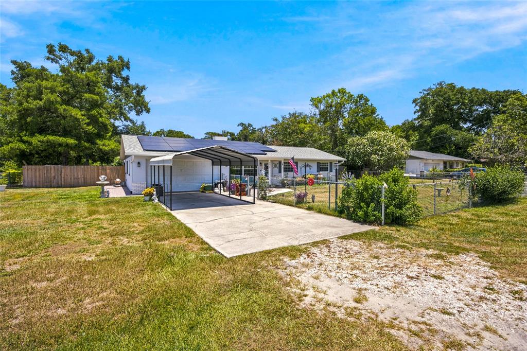 A single-story house with a carport, solar panels, and a fenced yard under a blue sky — 2009 NE 49TH STREET, OCALA, FL