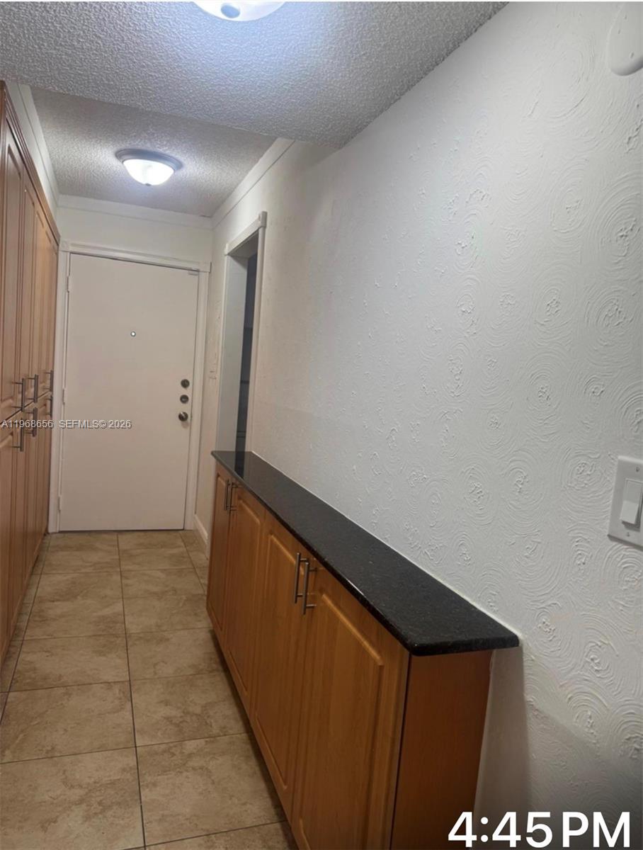A hallway features tile flooring, wood cabinetry with a black countertop, and textured white walls — 3110 N Pine Island Rd # 110, Sunrise FL 33351, SUNRISE, FL