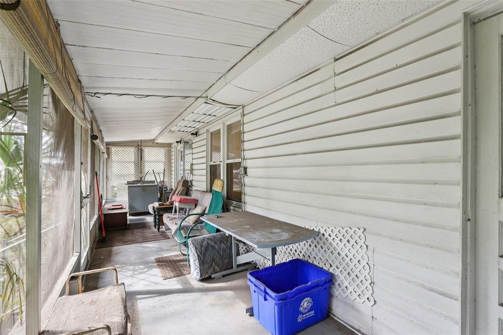 A screened-in porch with white horizontal siding, a concrete floor, and various pieces of furniture — 38025 13TH AVENUE, ZEPHYRHILLS, FL
