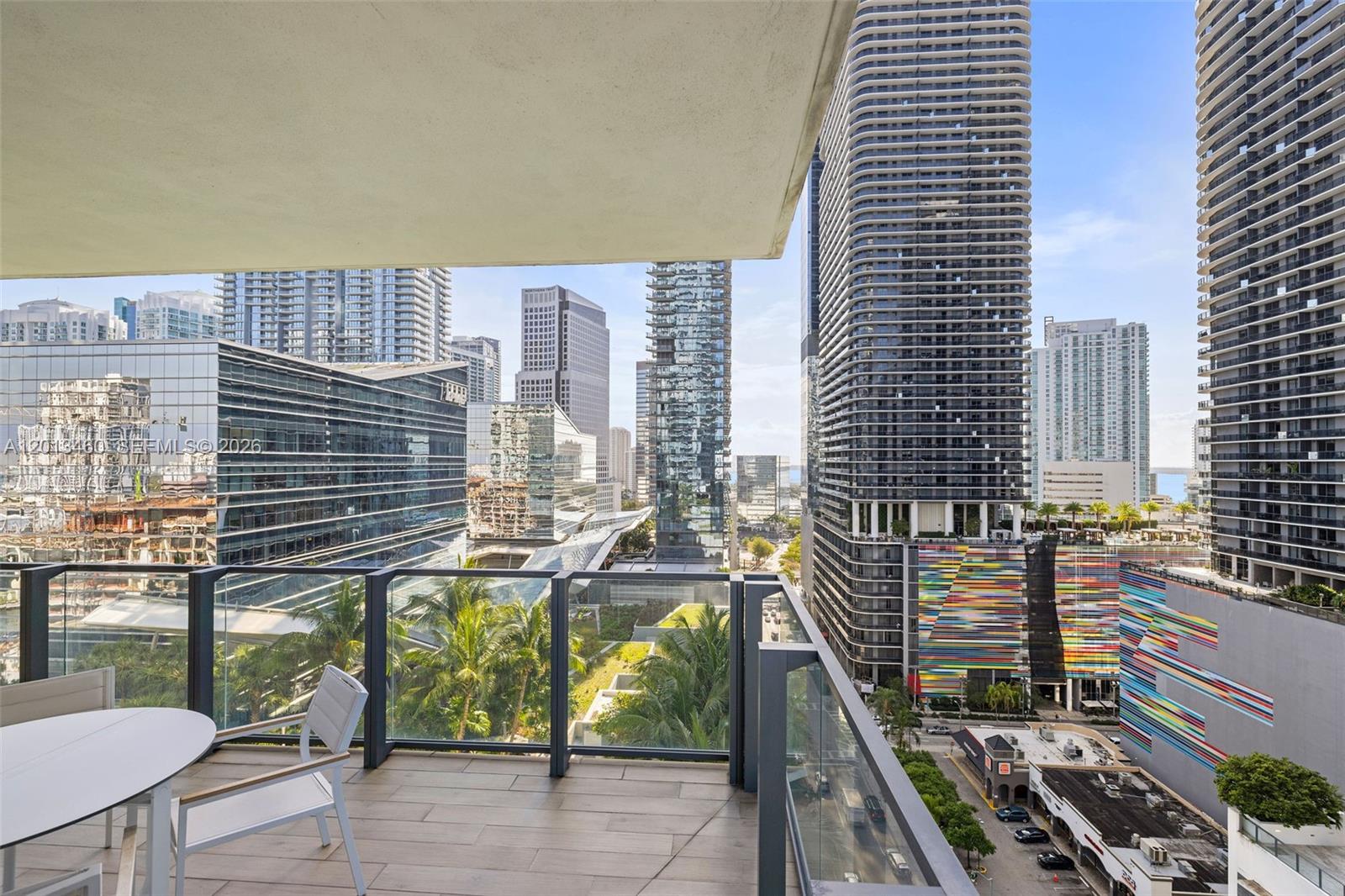 A balcony with a table and chairs overlooks a dense urban skyline with tall buildings — 88 SW 7th St # 1201, Miami FL 33130, MIAMI, FL