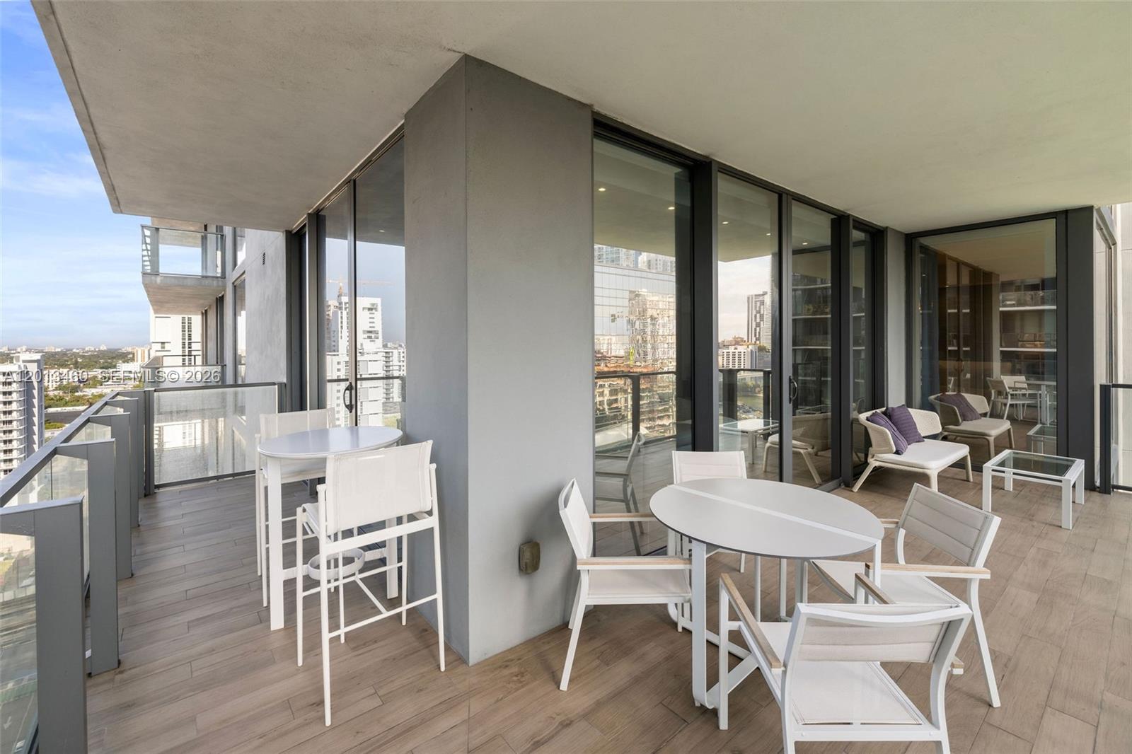 A modern balcony features outdoor dining sets, glass railings, and views of surrounding city buildings — 88 SW 7th St # 1201, Miami FL 33130, MIAMI, FL