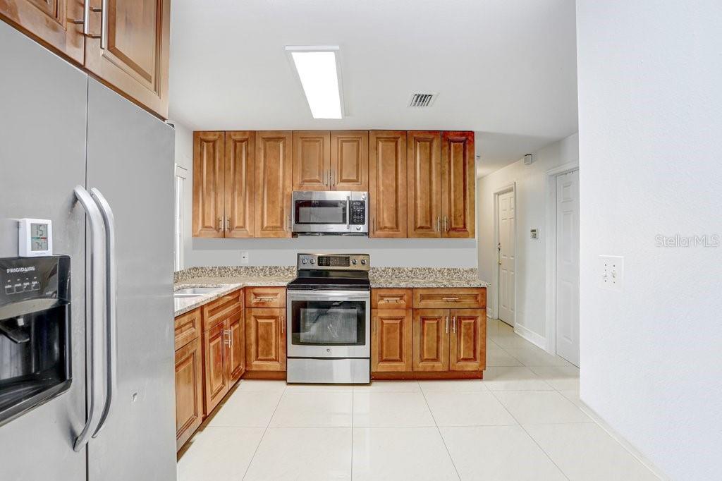 A kitchen features wood cabinets, granite countertops, stainless steel appliances, and light-colored tile flooring — 6923 N HIMES AVENUE, TAMPA, FL