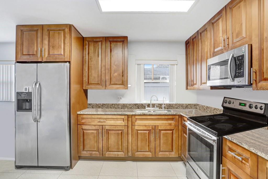 A kitchen with wood cabinets, granite countertops, stainless steel appliances, and a window above the sink — 6923 N HIMES AVENUE, TAMPA, FL