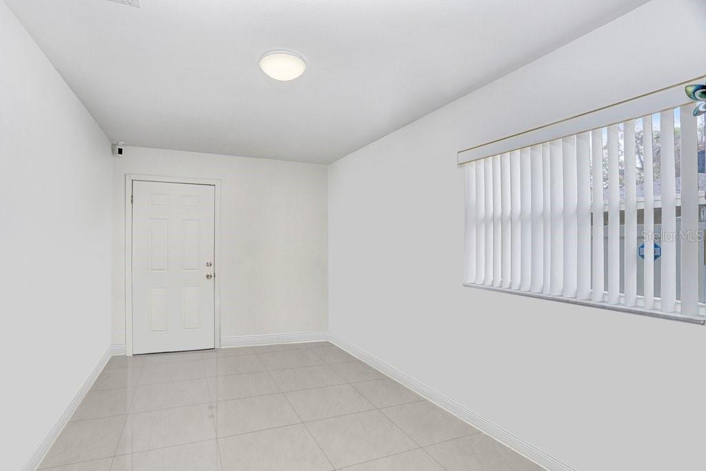 An empty room with white walls, light tile flooring, a white door, and vertical blinds — 6923 N HIMES AVENUE, TAMPA, FL