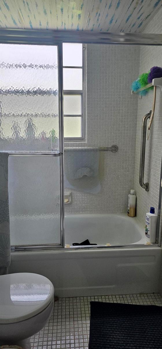 A bathroom features a white bathtub with sliding glass doors, tiled walls, and a grab bar — 263 Suffolk G, Boca Raton FL 33434, BOCA RATON, FL