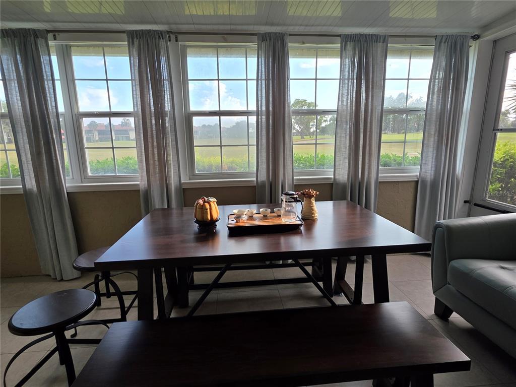 A sunroom features a dark wood dining table, benches, and large windows overlooking a golf course — 3607 AVENIDA MADERA UNIT B, BRADENTON, FL