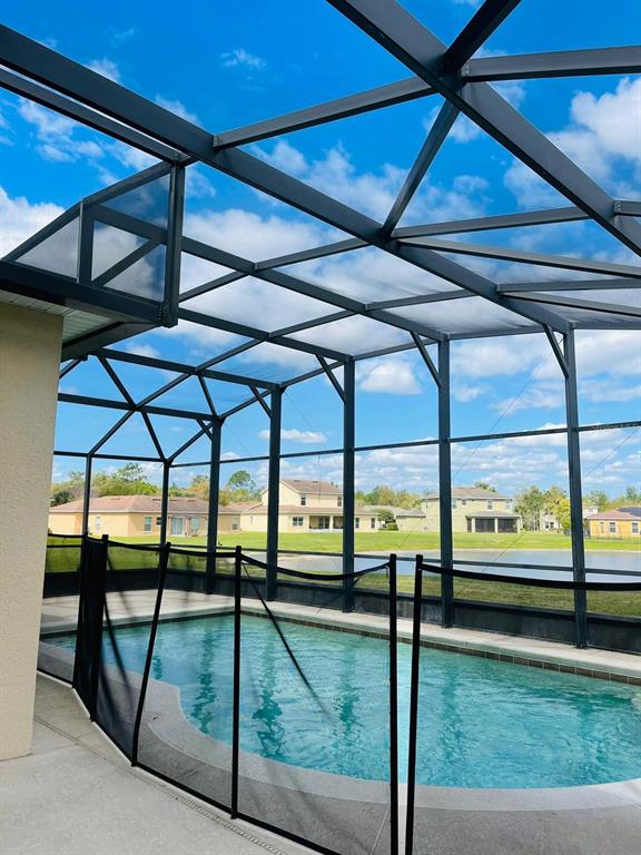 A swimming pool with a safety fence is enclosed by a screened lanai overlooking houses — 3603 LIGHT PORT WAY, KISSIMMEE, FL