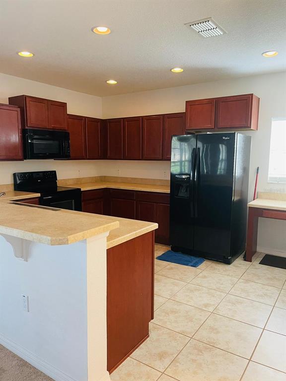 A kitchen features dark wood cabinets, black appliances, and light-colored countertops — 3603 LIGHT PORT WAY, KISSIMMEE, FL