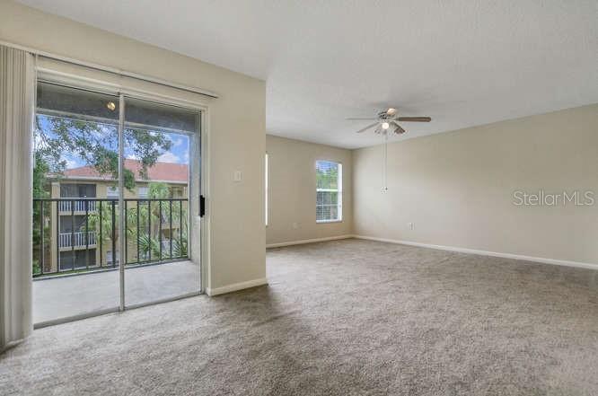 A carpeted living room features a ceiling fan and a sliding glass door to a balcony — 2690 CORAL LANDINGS BOULEVARD UNIT 438, PALM HARBOR, FL