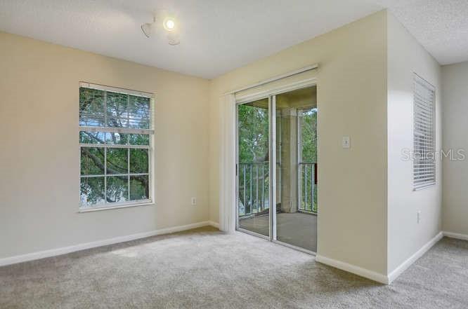 An empty room with beige carpet, a window, and a sliding glass door to a balcony — 2690 CORAL LANDINGS BOULEVARD UNIT 438, PALM HARBOR, FL